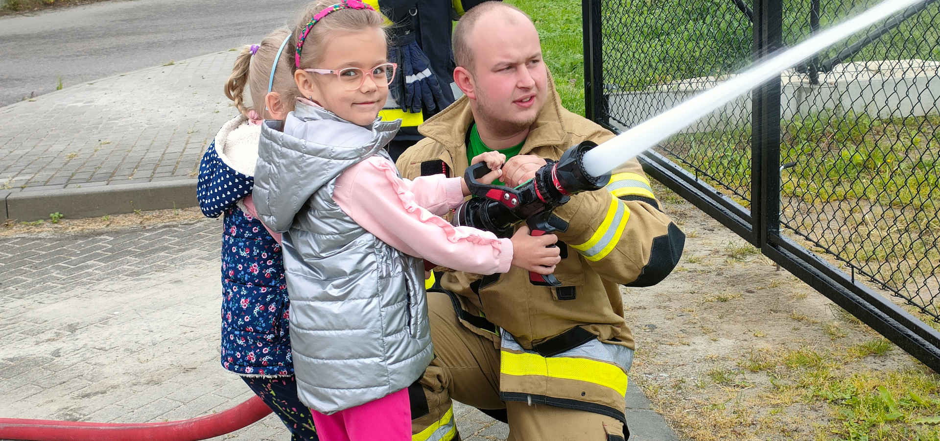 Dziewczynka wraz ze strażakiem trzyma wąż strażacki