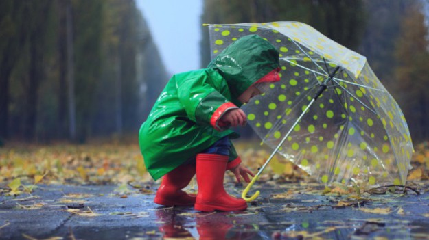 Dziecko w zielonym płaszczu przeciwdeszczowym z przezroczystą parasolką